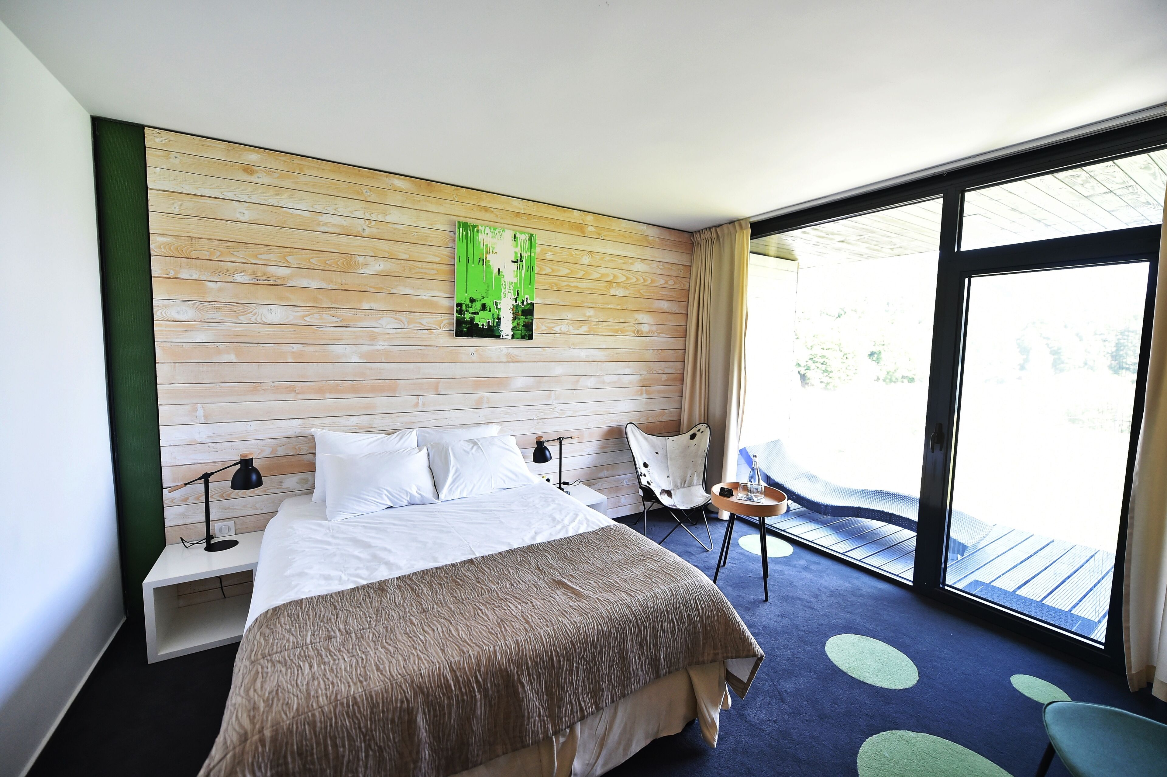 A hotel room with a bed, a chair, a small table, and a large window.