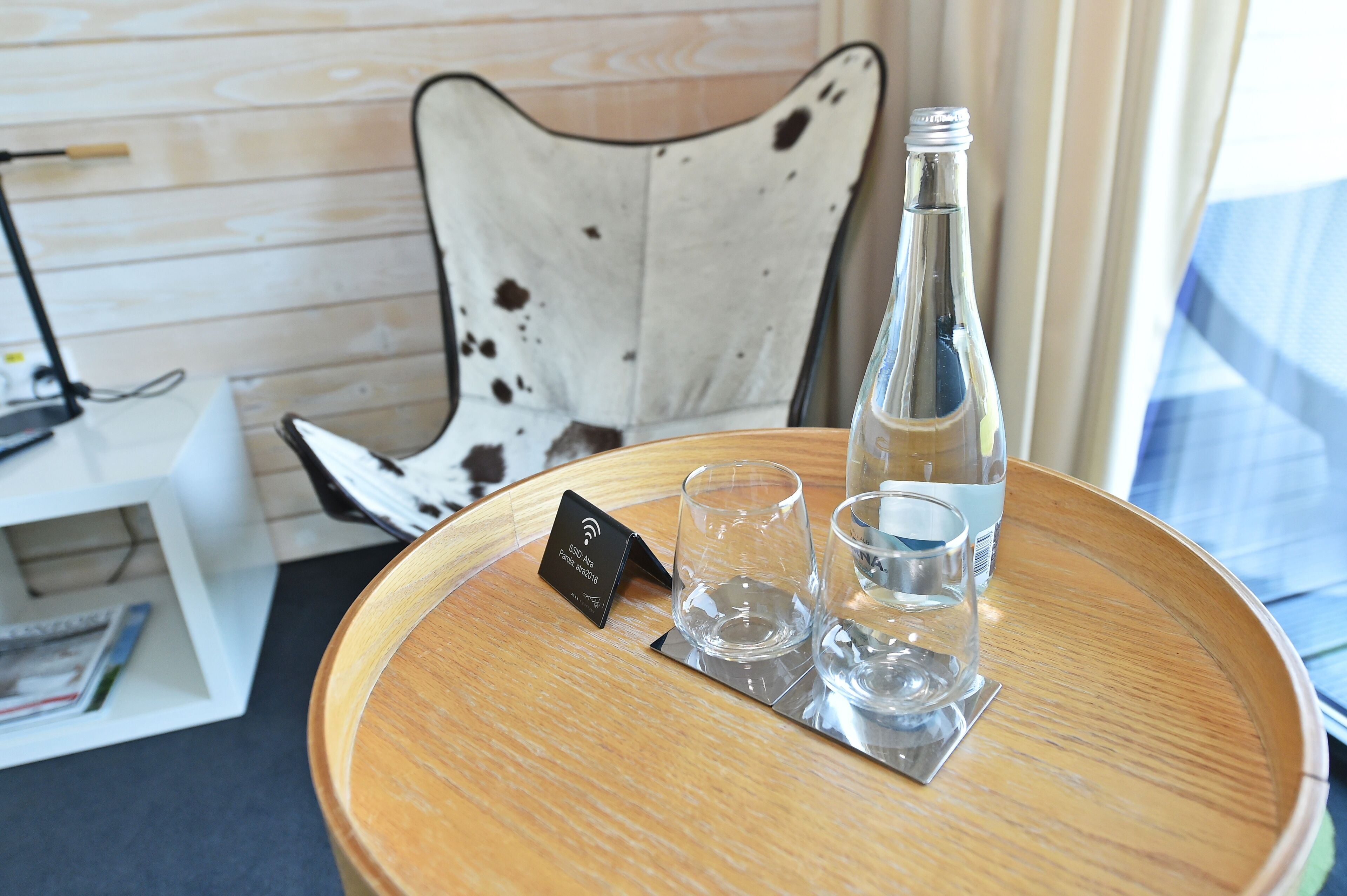 Une table ronde en bois, avec une bouteille et deux verres dessus.
