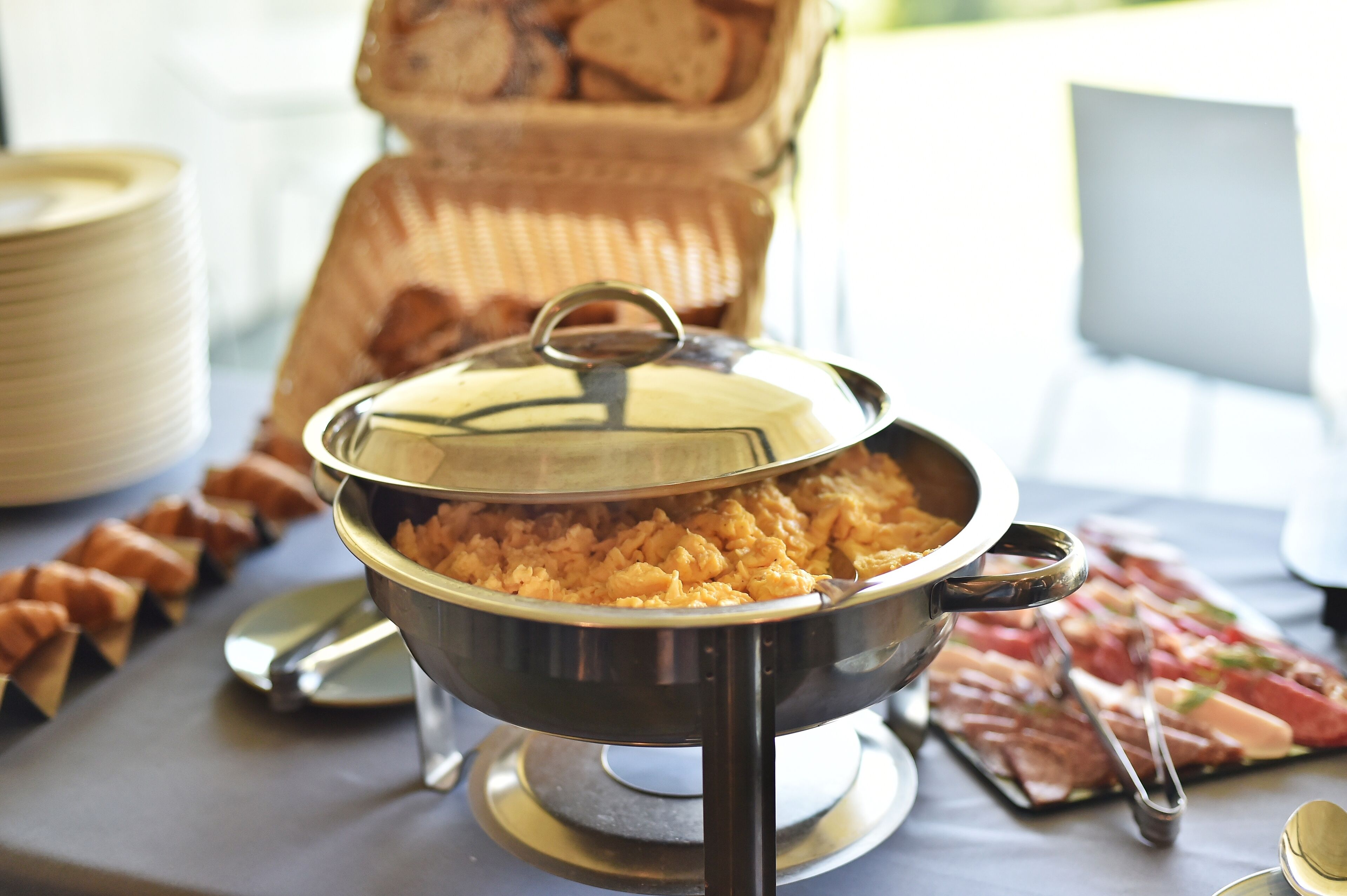 A buffet table with a covered dish of food, a tray of sliced meats, and a stack of plates.