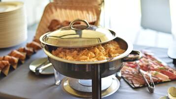 A buffet table with a covered dish of food, a tray of sliced meats, and a stack of plates.