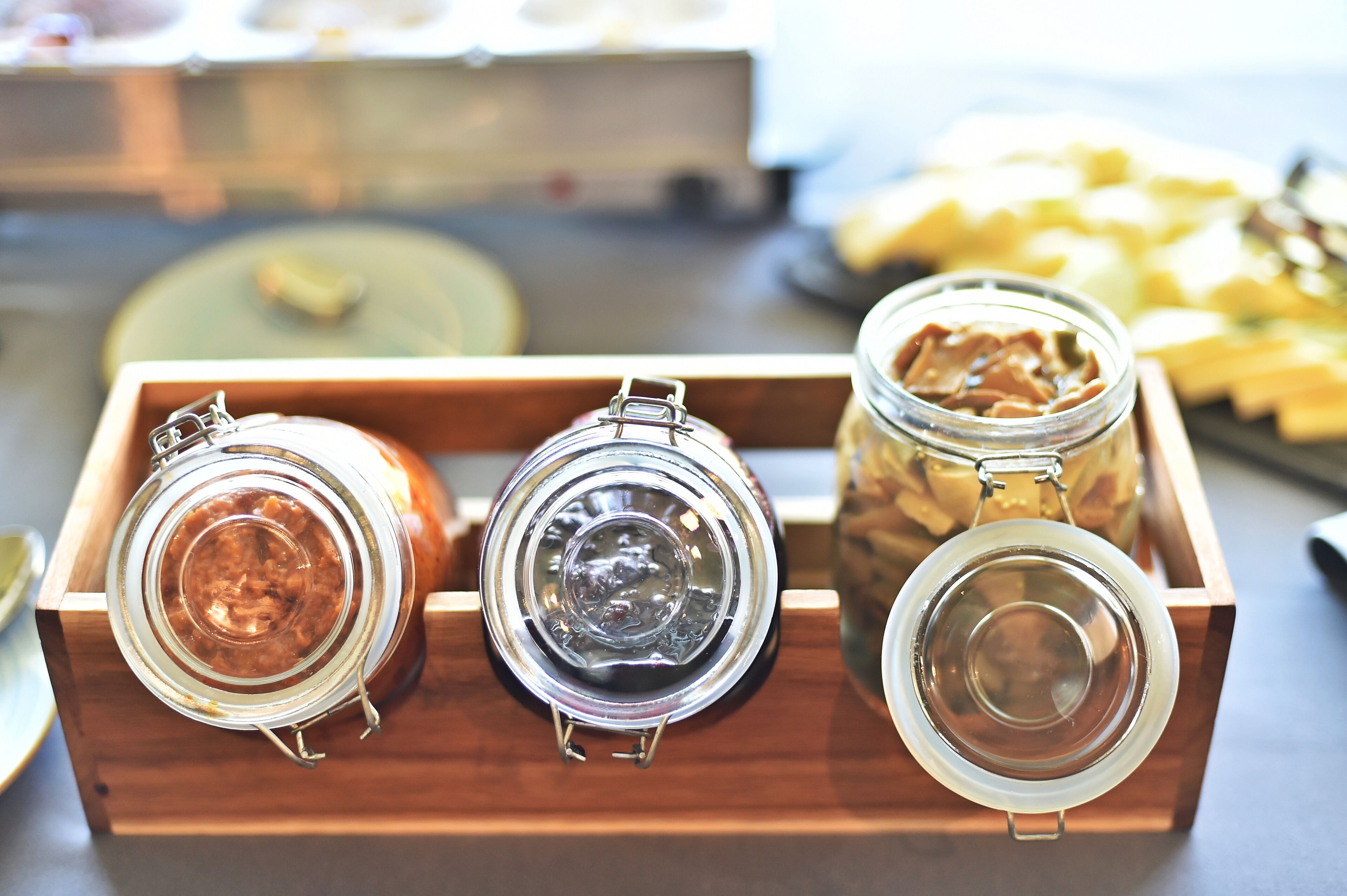 A wooden tray with three glass jars containing different spreads.