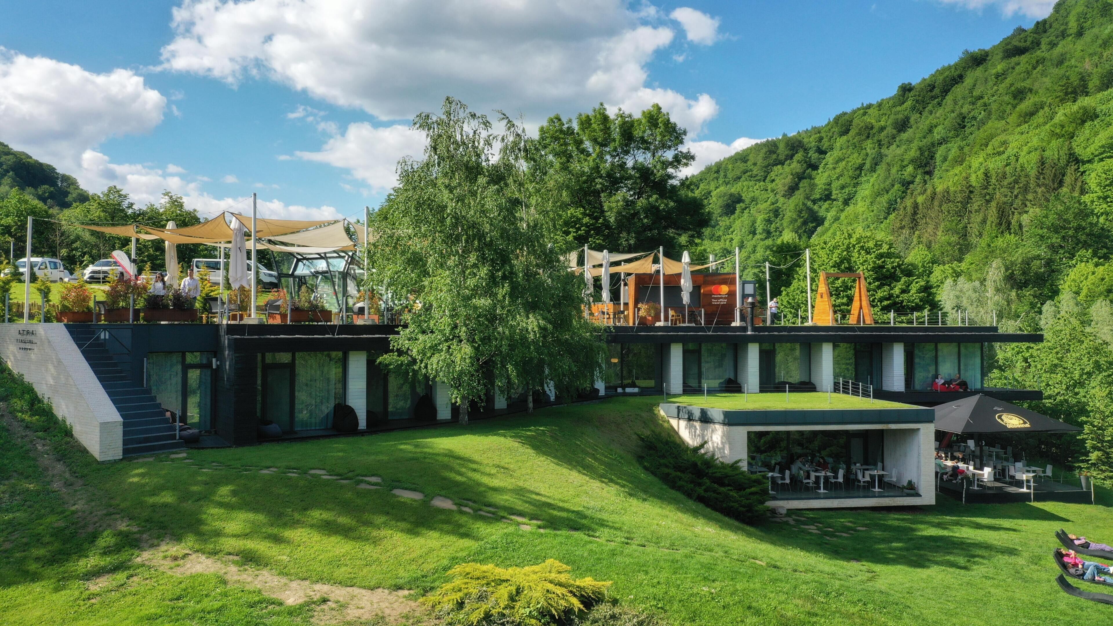 A modern building with a glass facade, outdoor seating, and a grassy area.