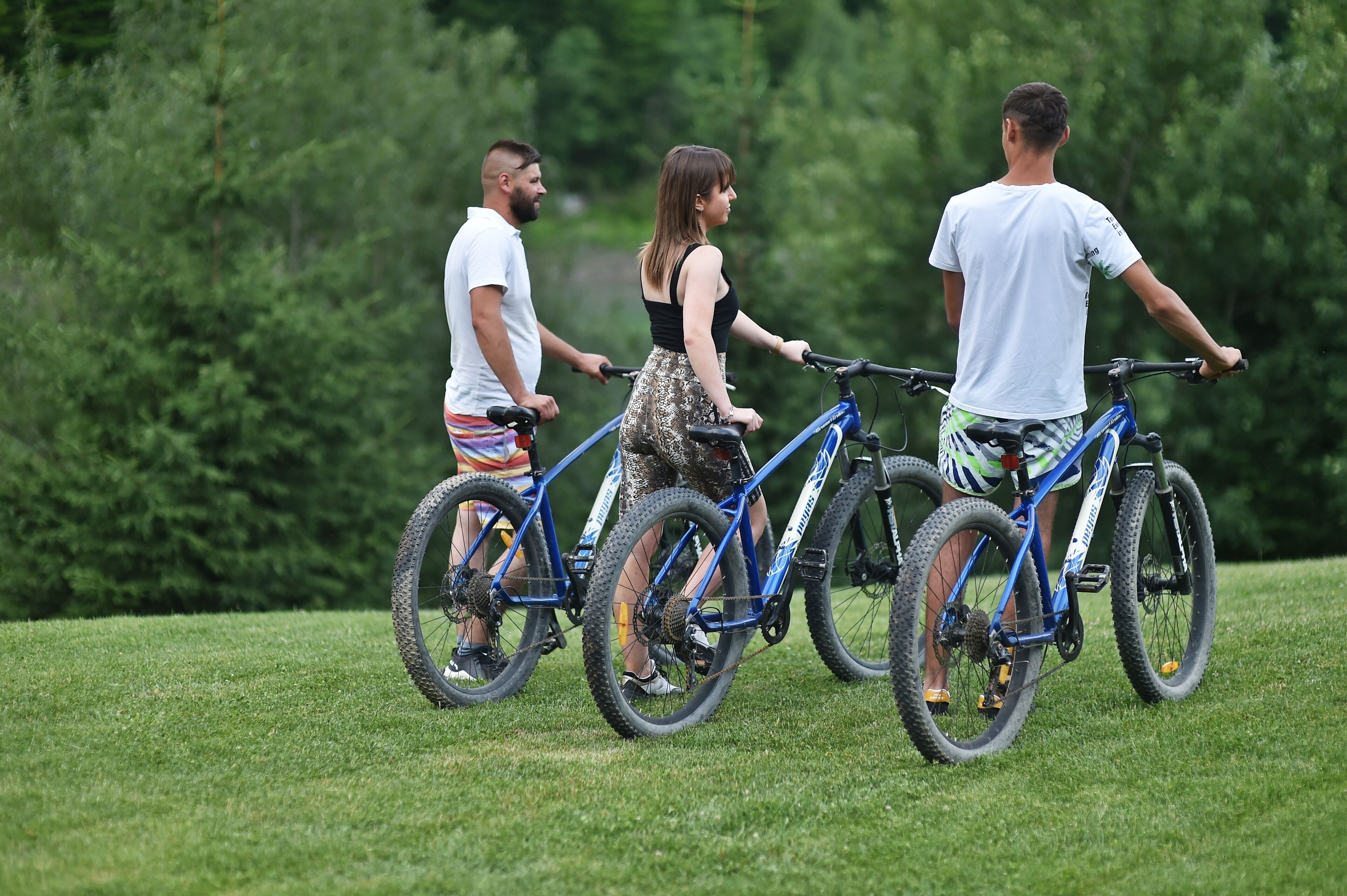 Three people on bicycles in a grassy area with trees in the background.