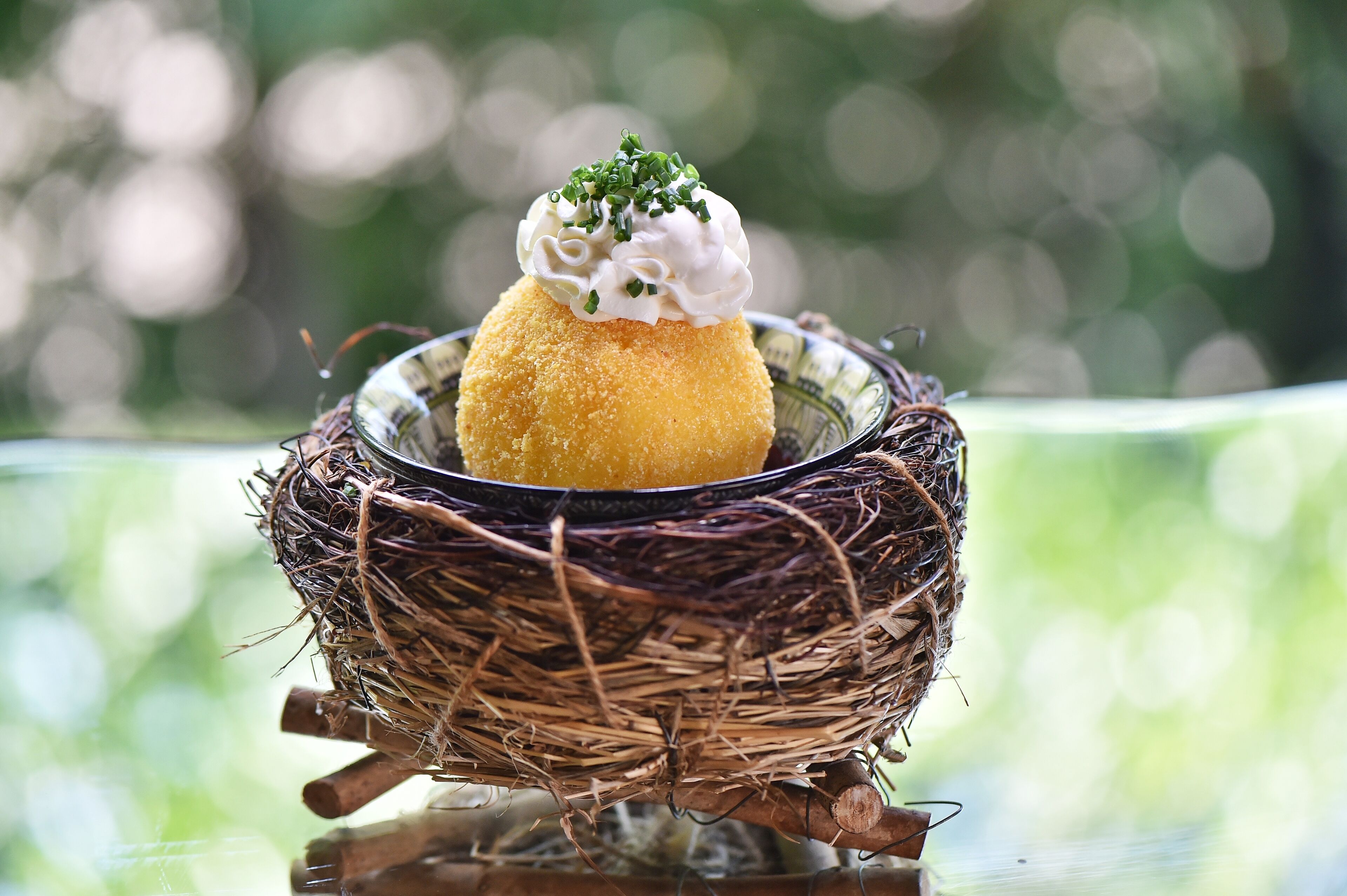 Recipiente con forma de nido que contiene un alimento con una cucharada de crema y un adorno verde.