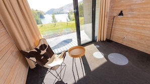 Un balcón con vista a un lago, una silla, una mesita y una lámpara de pie.
