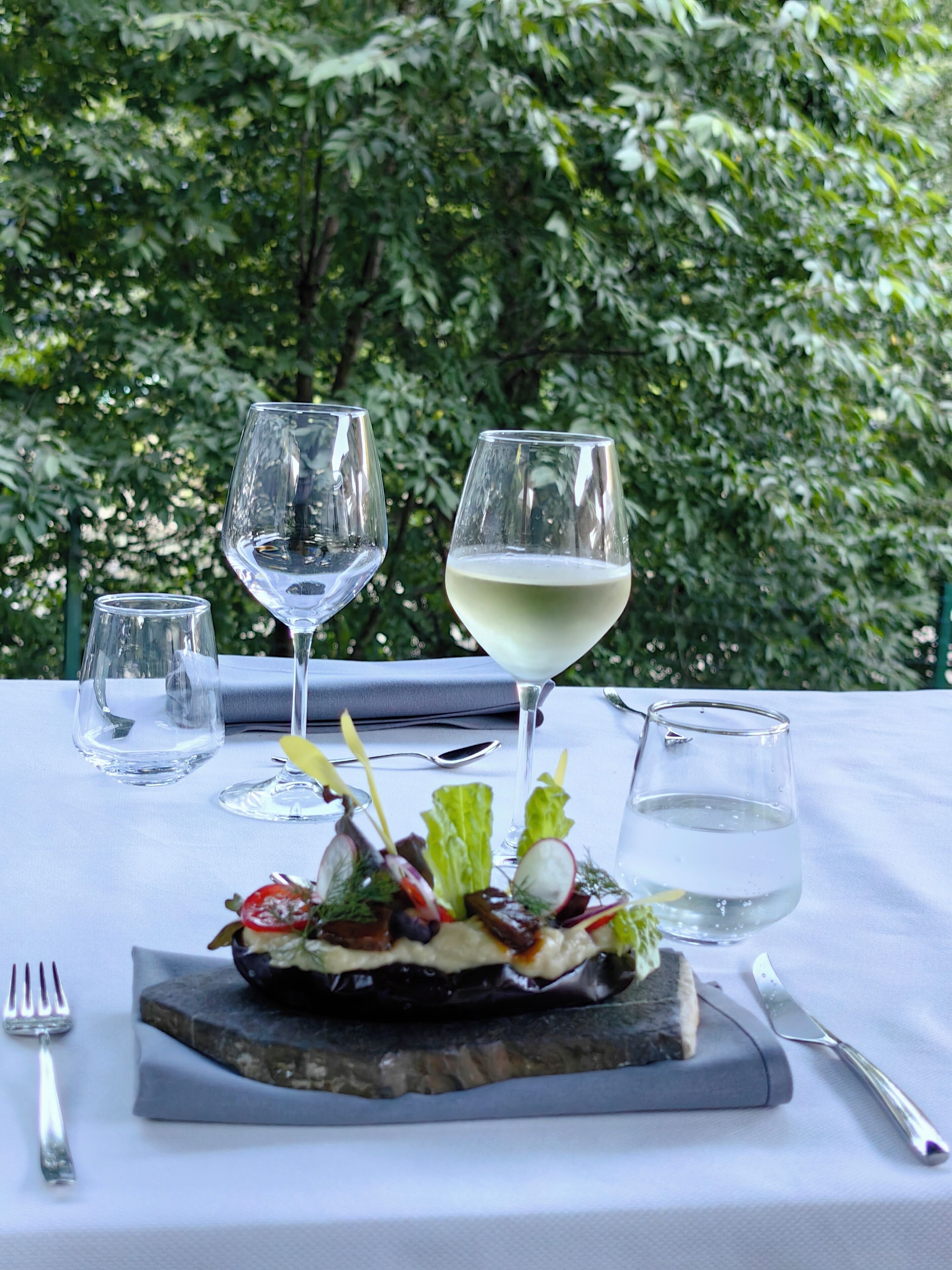 Une table dressée avec un verre de vin blanc, un verre d’eau et une assiette de nourriture.