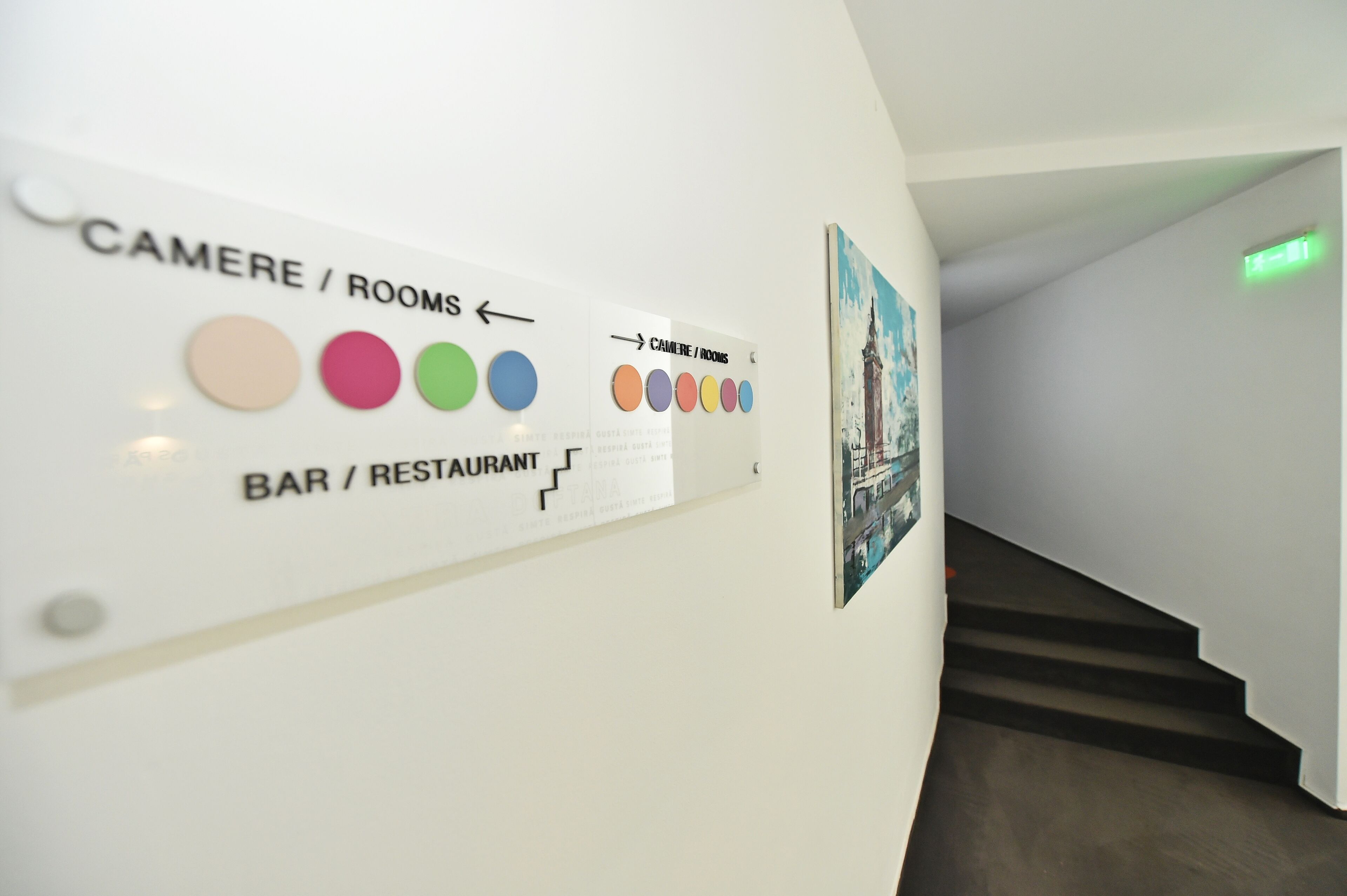 A wall with directional signs indicating 'CAMERE / ROOMS' and 'BAR / RESTAURANT' with corresponding color-coded circles.