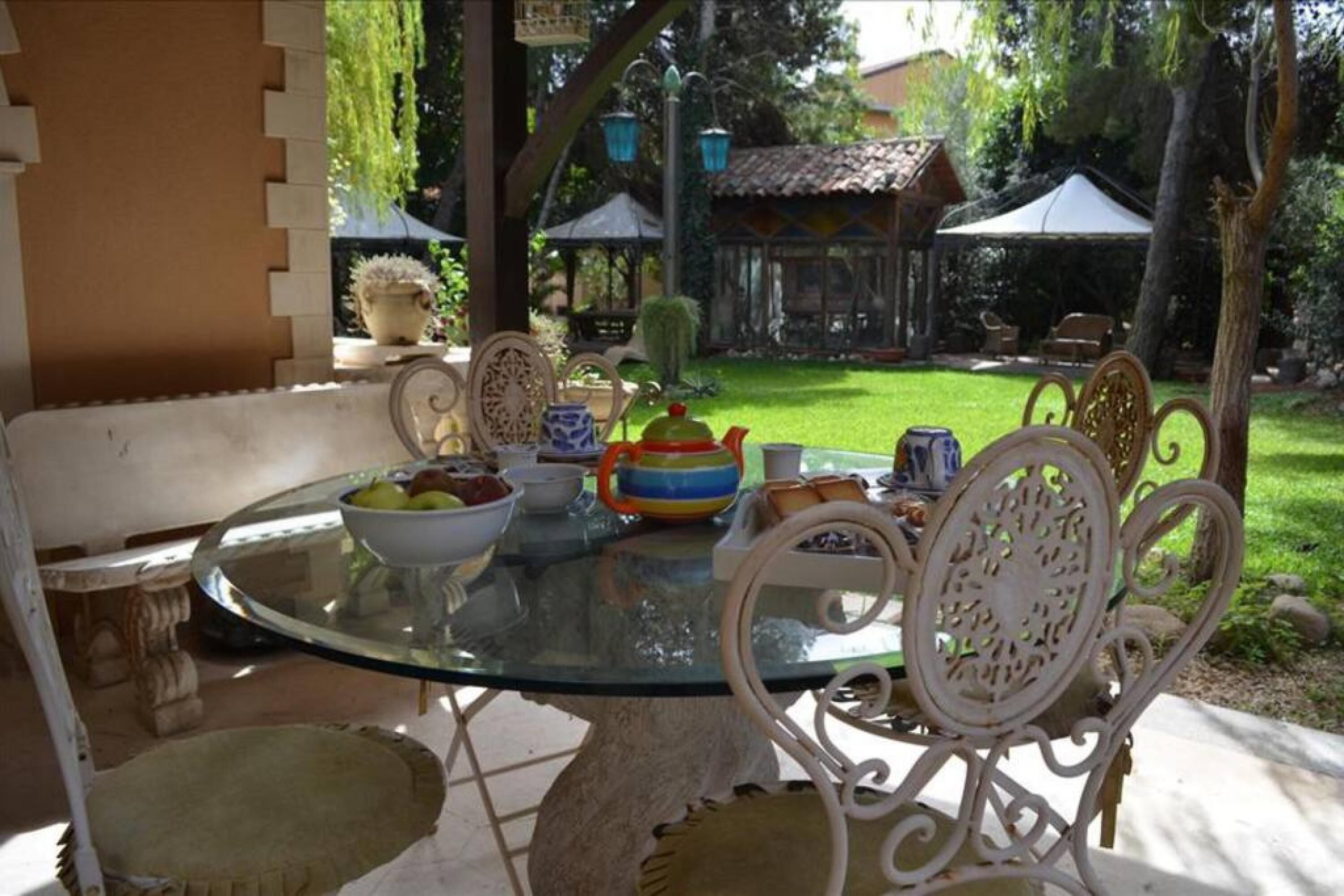 A glass-top table with chairs, a bowl of fruit, and a teapot.