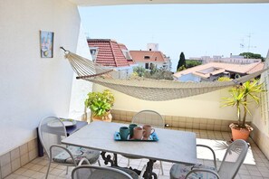 Un balcon avec une table, des chaises, un hamac et des plantes en pot.