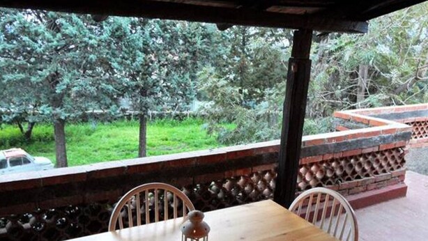 A wooden table with two chairs and a lantern under a roofed area with a view of trees and a car in the background. - Villa Bonaccorso - Il Casotto il Limone Verde (Viagrande)