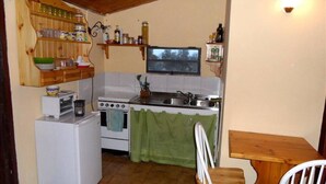 A compact kitchen with a stove, sink, and a small refrigerator. There is a wooden chair and a table with a chair. - Villa Bonaccorso - Il Casotto il Limone Verde (Viagrande)