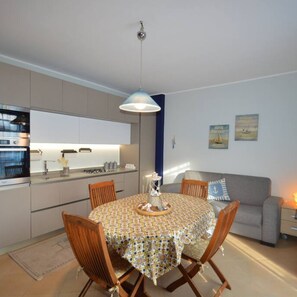 A modern kitchen with a dining area, a sofa, and artwork on the wall. - Appartamento Orchidea in Residence con Piscina Condominiale (Mascali)