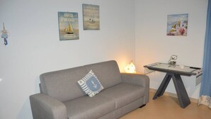 A living room with a grey sofa, a small table with a lamp, and nautical-themed wall art. - Appartamento Orchidea in Residence con Piscina Condominiale (Mascali)