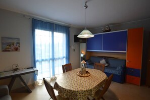 A compact living space with a round dining table, a sofa, and a kitchenette area. - Appartamento Orchidea in Residence con Piscina Condominiale (Mascali)