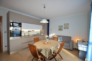 A modern kitchen with built-in appliances, a dining table with chairs, and a sofa in a living area. - Appartamento Orchidea in Residence con Piscina Condominiale (Mascali)