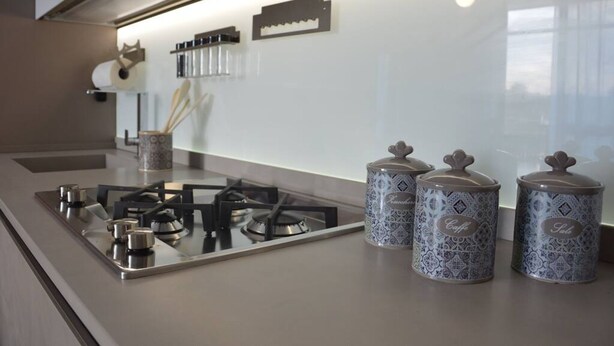 A modern kitchen with a gas stove, a coffee maker, and decorative jars on the counter. - Appartamento Orchidea in Residence con Piscina Condominiale (Mascali)