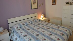 A bedroom with a bed, a nightstand, a dresser, and a wall-mounted light fixture. - Appartamento Orchidea in Residence con Piscina Condominiale (Mascali)