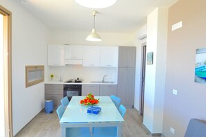 Uma cozinha moderna com armários brancos, uma mesa azul com cadeiras e um lustre.