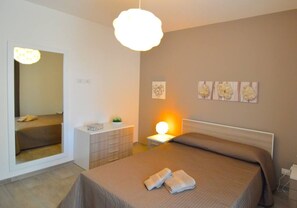 Quarto com cama, mesa de cabeceira, luminária e decoração na parede.