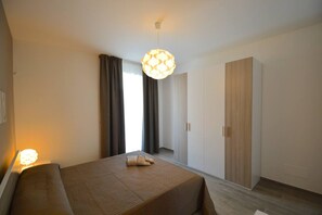 Quarto de hotel moderno com cama, guarda-roupa e uma janela grande com cortinas.