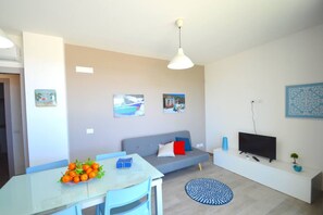Uma sala de estar moderna com uma mesa de jantar de vidro, um sofá cinza, uma televisão de tela plana e um tapete azul estampado.
