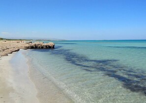 Une plage avec une eau claire et peu profonde, un promontoire rocheux et une côte visible au loin.