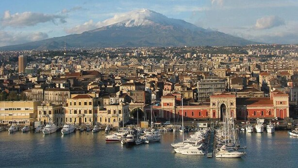 A coastal cityscape with a marina filled with boats, historic buildings, and a prominent mountain in the background.