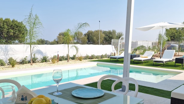 A poolside dining area with a table set for two, a glass of water, and a plate of lemons. - Villa Elisia - Villetta con Piscina Privata (Augusta)