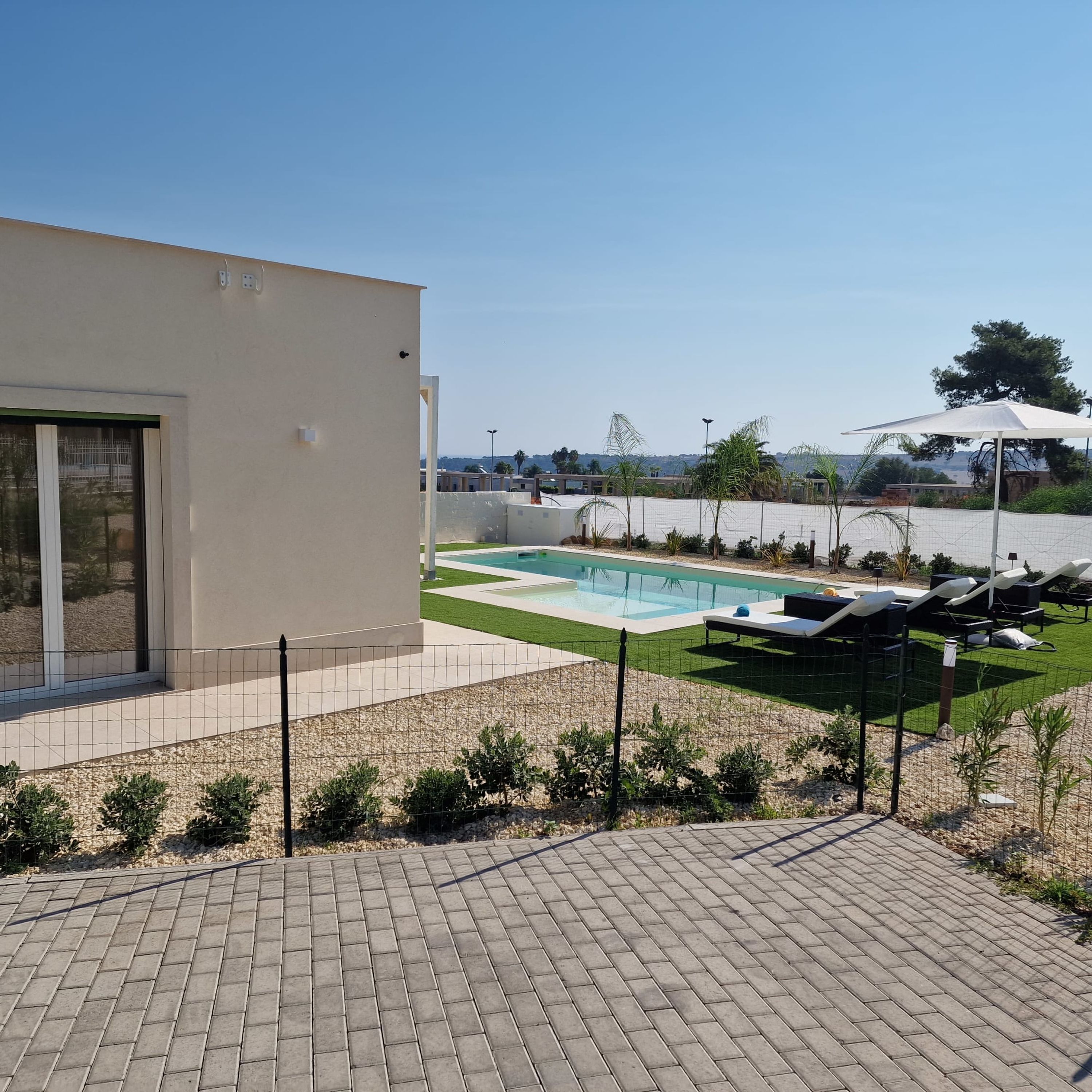 Un área de piscina exterior moderna con vista despejada, sillas de descanso y un césped bien cuidado.