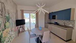A modern kitchen with a dining area, featuring a cactus mural, a flat-screen TV, and a unique ceiling light fixture. - Villa Elisia - Villetta con Piscina Privata (Augusta)