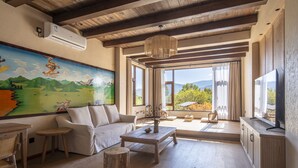 A spacious living room with a large painting, a sofa, a coffee table, and a view of the outdoors. - Shujia wengmacuozangshidujiazhuangyuan (Deqin)