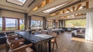 A spacious living area with a large wooden table, multiple seating options, and large windows offering a view of the outdoors. - Shujia wengmacuozangshidujiazhuangyuan (Deqin)