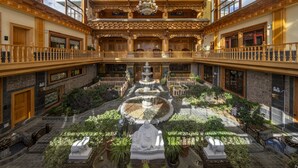 A spacious atrium with a central fountain, multiple balconies, and a variety of indoor plants. - Shujia wengmacuozangshidujiazhuangyuan (Deqin)