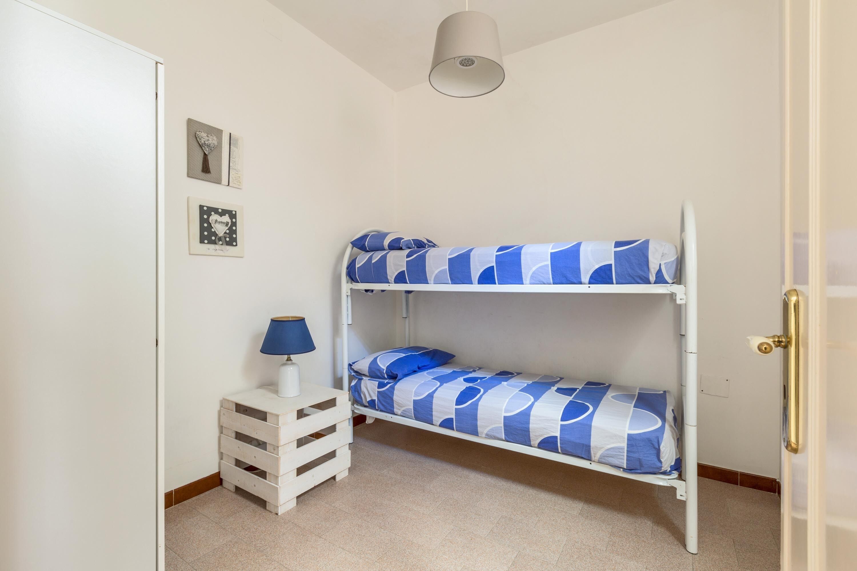 Una cama nido con una colcha azul y blanca estampada, una mesita de noche con una lámpara y una puerta blanca.