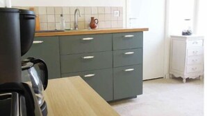 A kitchen with a wooden table, a coffee machine, a sink, and a cabinet.