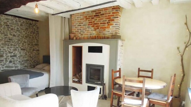 A cozy living room with a stone wall, a fireplace, a round table with chairs, and a sofa.