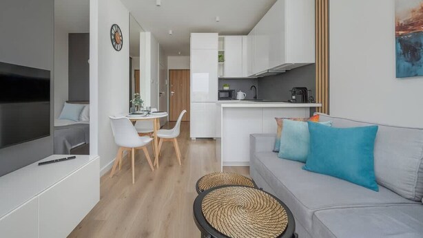 A modern living space with a dining area, kitchenette, and a gray sofa with blue cushions.