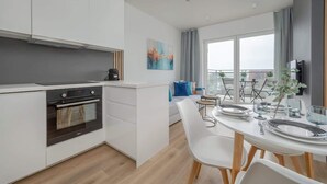 A modern kitchen with white cabinetry, a built-in oven, and a dining area with a white table and chairs.