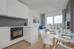 A modern kitchen with white cabinetry, a built-in oven, and a dining area with a white table and chairs.