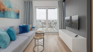 A modern living room with a sofa, two small tables, a TV, and a balcony with chairs.