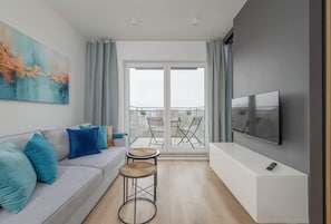 A modern living room with a sofa, two small tables, a TV, and a balcony with chairs.