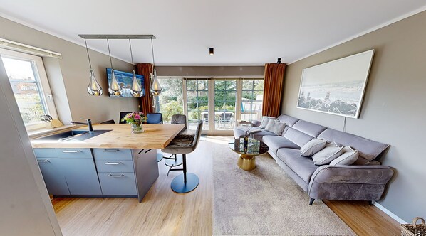 A modern kitchen with a central island, a dining area with a sofa and table, and a large window with curtains.