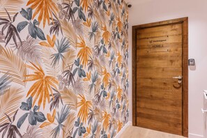 Una habitación con una puerta de madera que indica “Checkmyguest HOME 2” y una pared con un estampado de hojas tropicales.