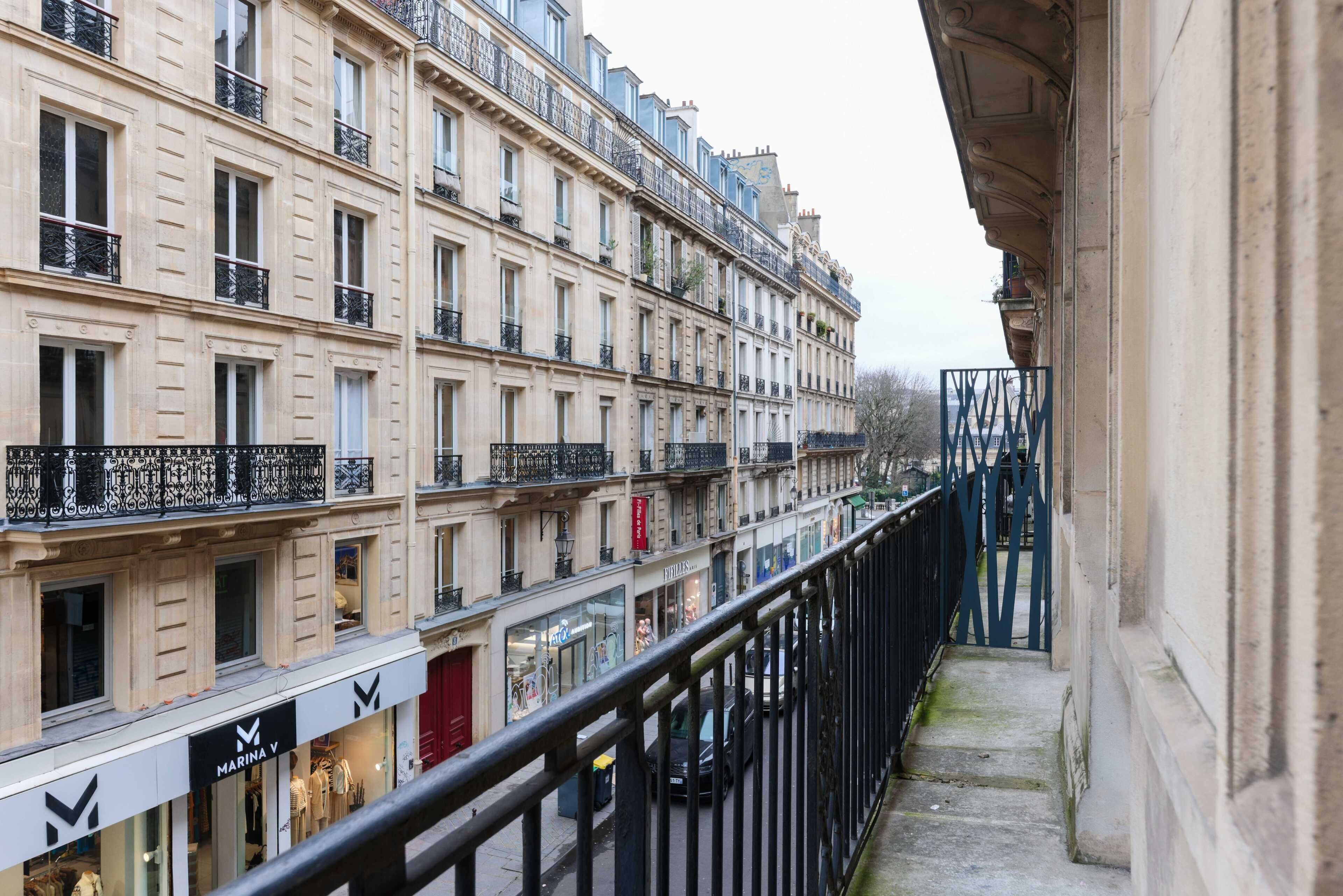 Une rangée d’immeubles à plusieurs étages dotés de balcons, une devanture de magasin avec une enseigne et une rambarde métallique le long du bord.