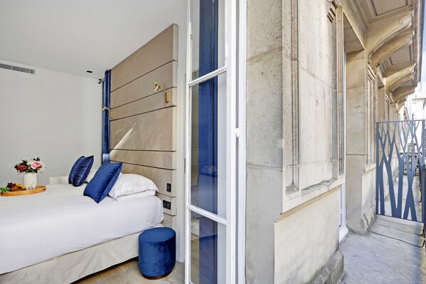 Un dormitorio con cama, una mesita de noche con un florero y una ventana con vista a la calle.