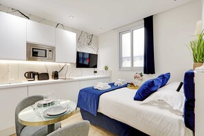 Una habitación de hotel moderna con cama, una pequeña mesa de comedor, microondas y televisor.