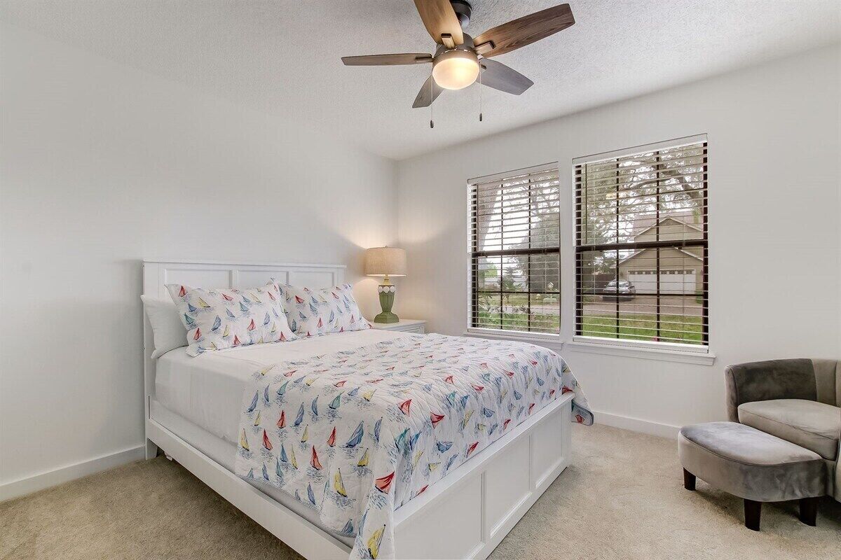 A bedroom with a bed, a ceiling fan, a window with blinds, and a chair.