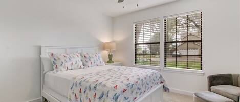 A bedroom with a bed, a ceiling fan, a window with blinds, and a chair.
