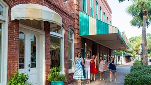 A group of people walking outside a building with a brick facade and a green awning.