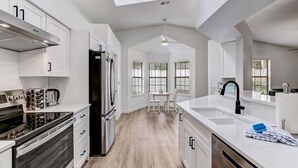 A modern kitchen with white cabinetry, a black refrigerator, and a large island with a sink.